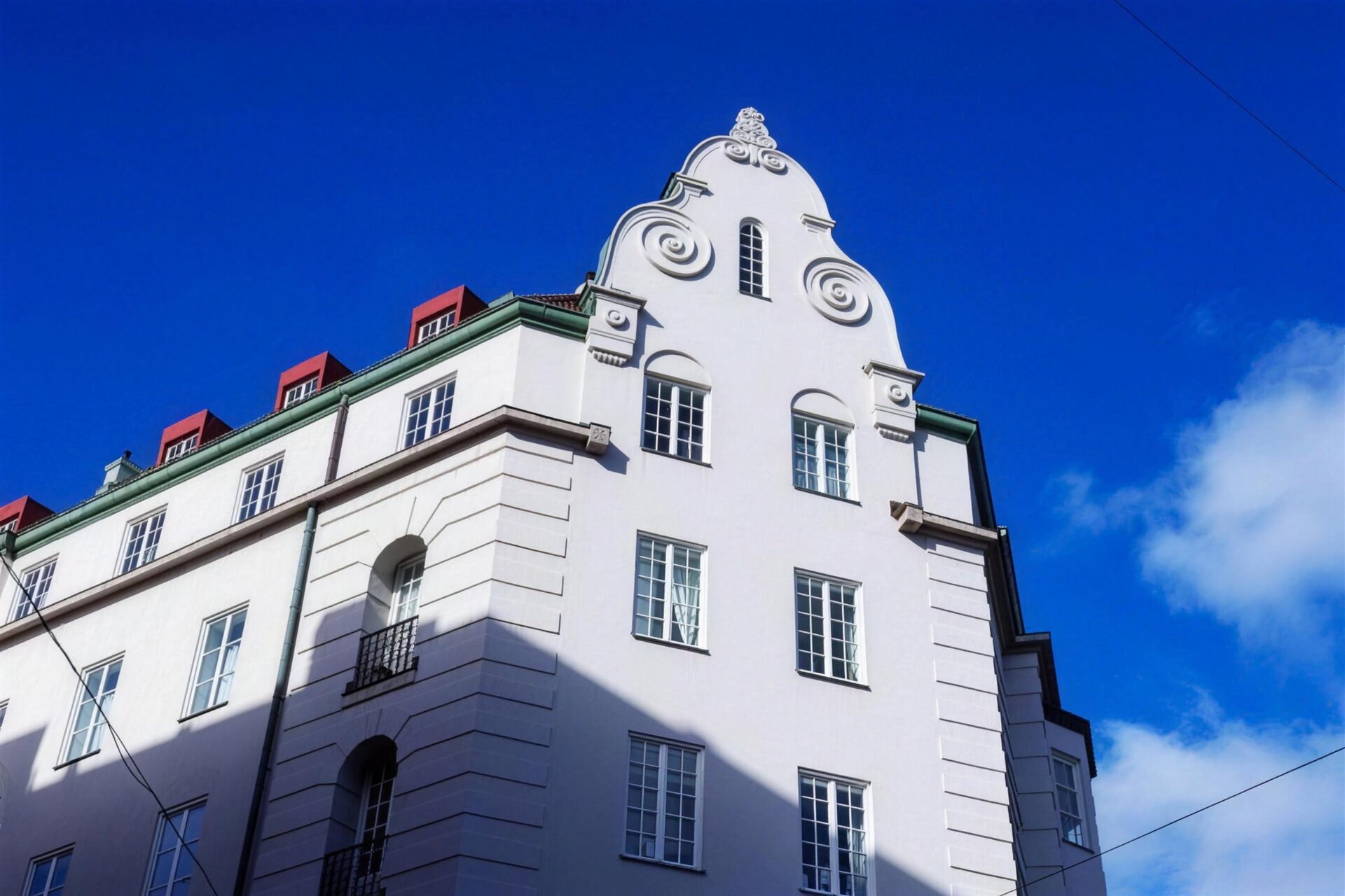 Vit putsfasad med dekorerad gavel mot blå himmel