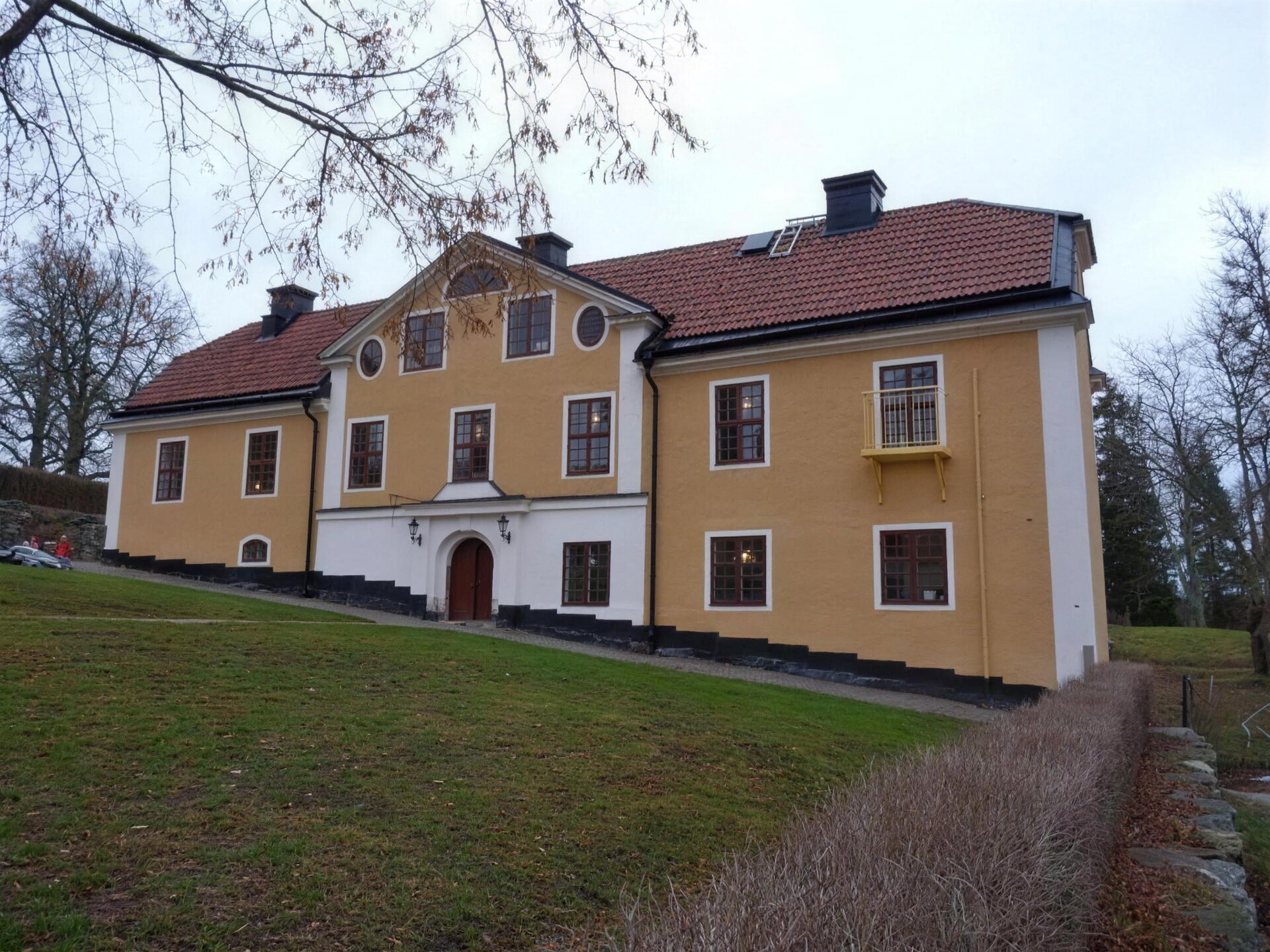 Gul herrgård med vita knutar i parkmiljö
